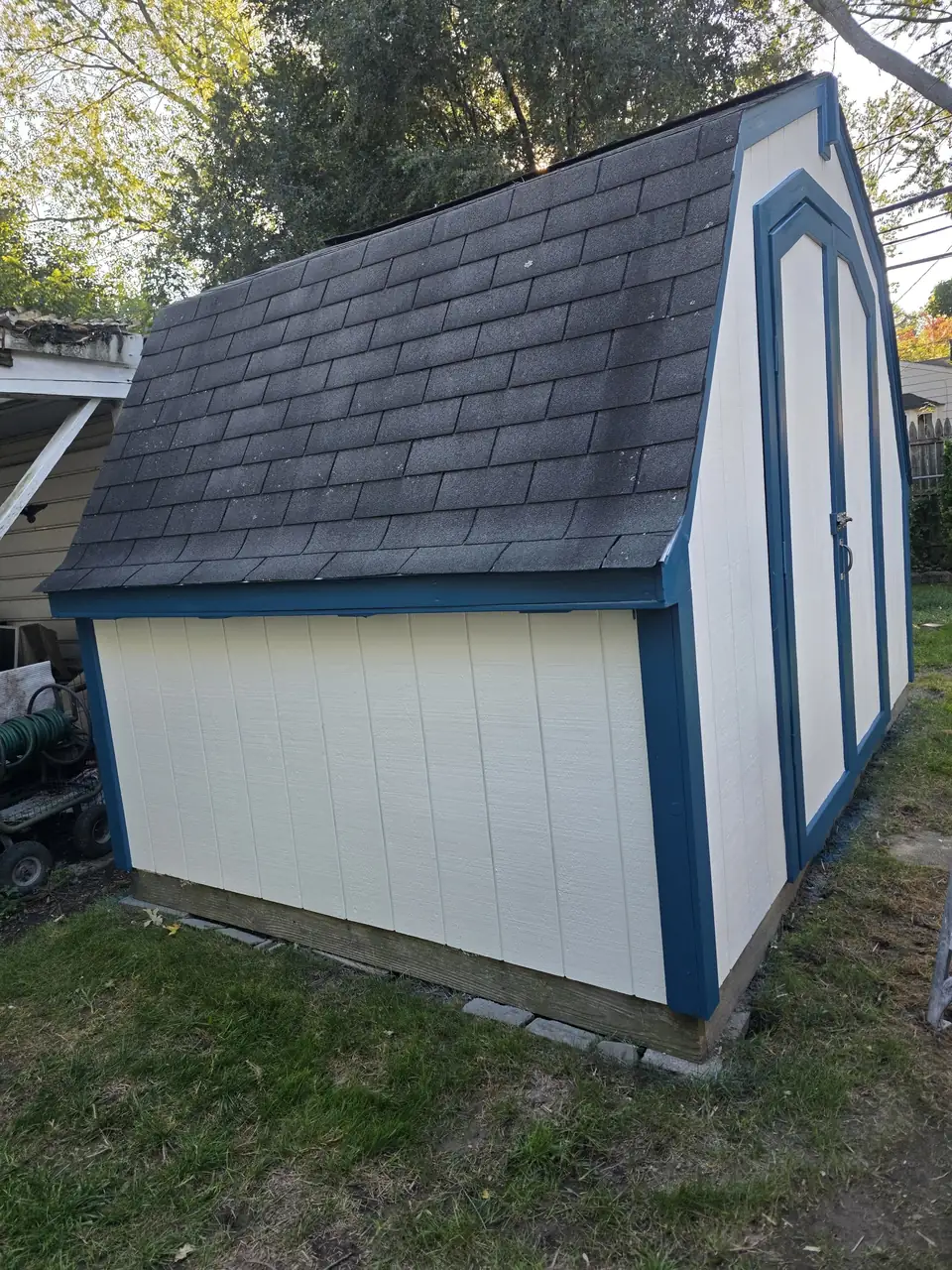 Backyard shed painted white with navy trim and doors
